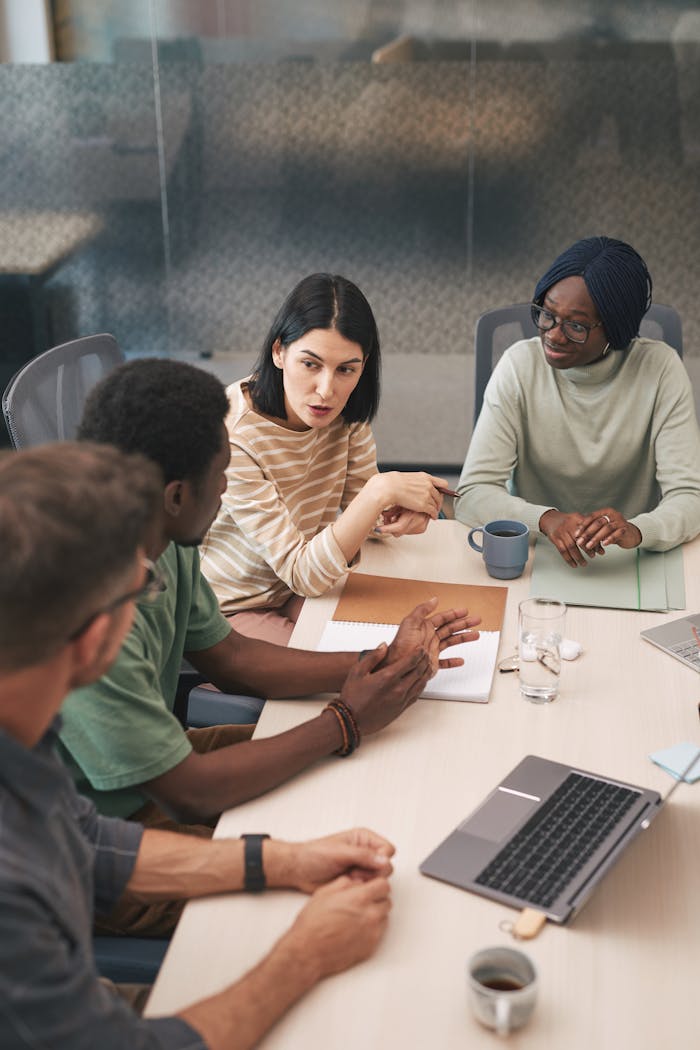 A diverse group of colleagues having an active meeting in a modern office setting with a laptop.